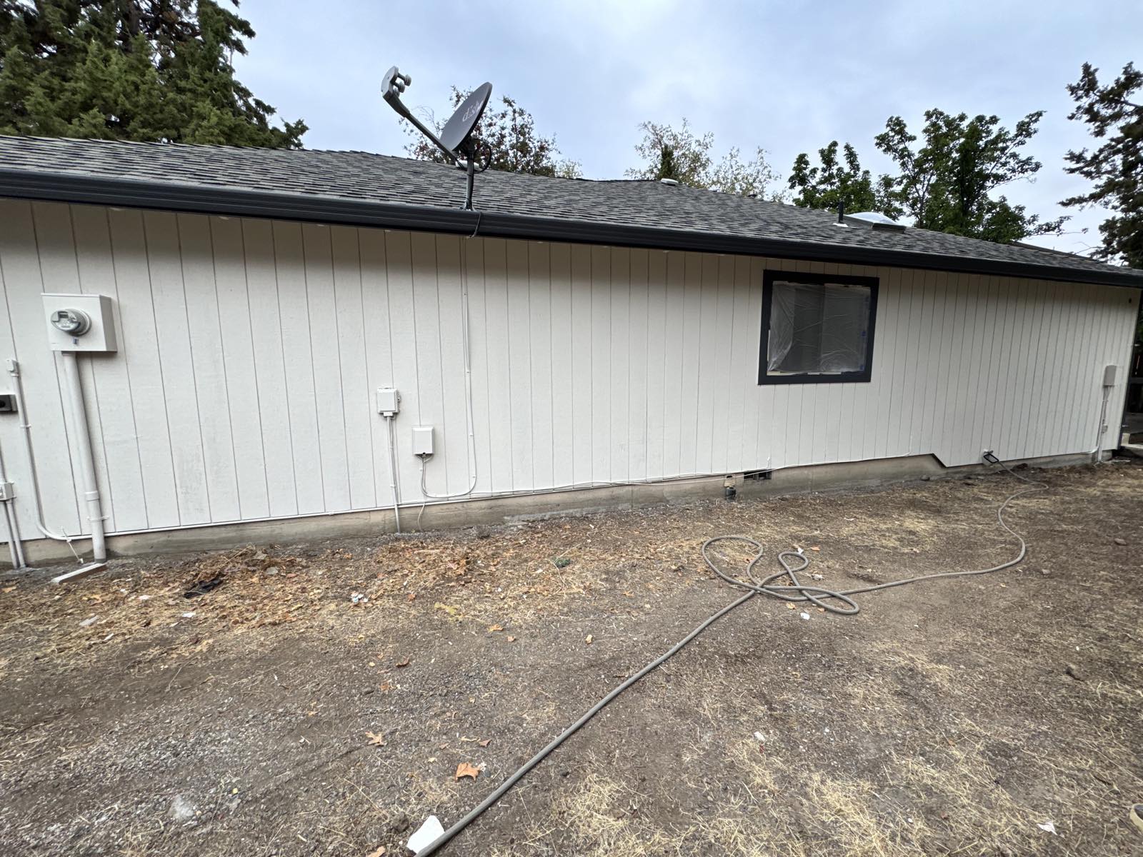 Side elevation of the same Bend, Oregon home with previously peeling vertical siding prepped and repainted off-white by Keystone Painting LLC, with charcoal gutters and fascia