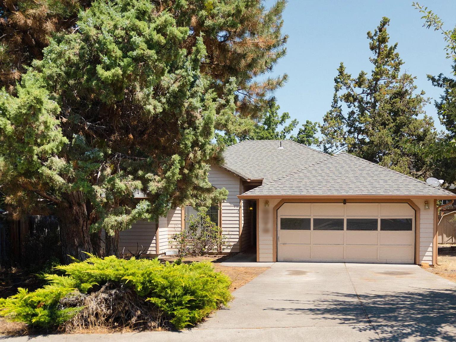 Front elevation of a Bend, Oregon ranch home before repainting, in a dated two-tone tan scheme with a single sheen and siding beginning to peel